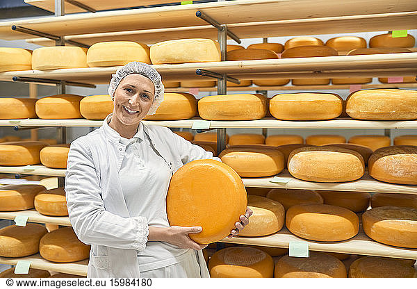 Cheese factory  smiling female worker holding cheese wheel