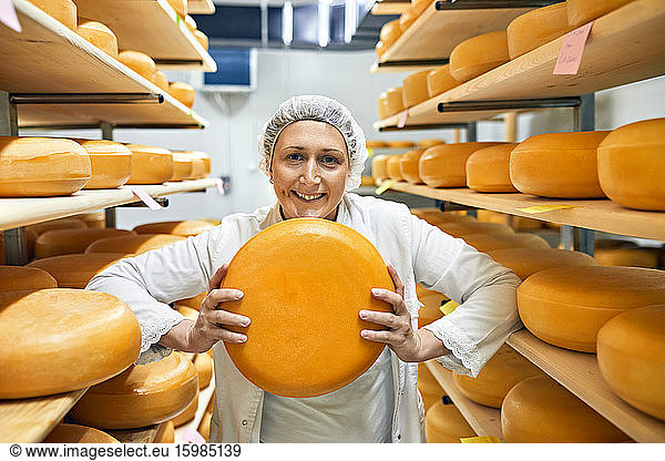 Cheese factory  smiling female worker with cheese wheel in storeroom