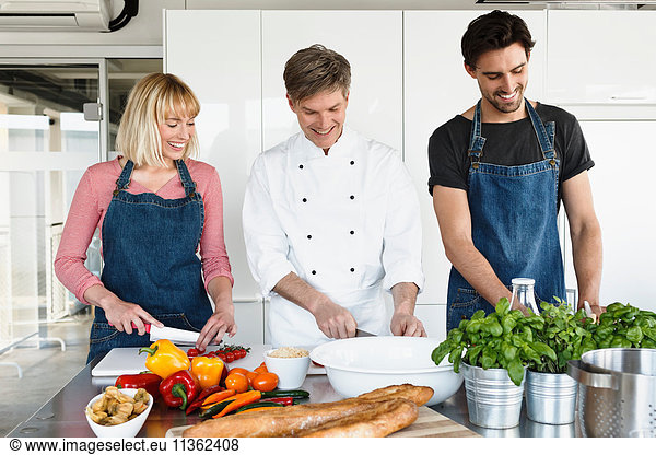 Chef and couple in kitchen slicing vegetables
