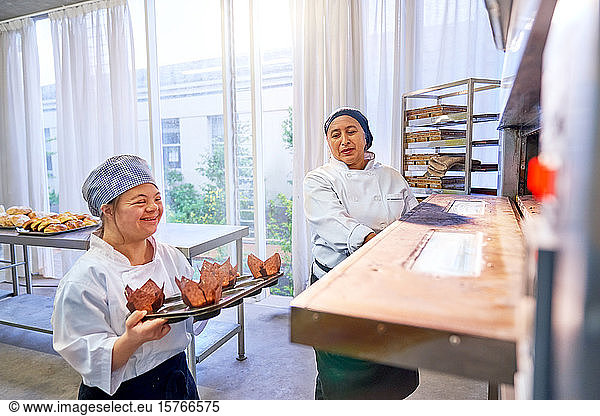 Chef and young woman with Down Syndrome placing muffins in oven