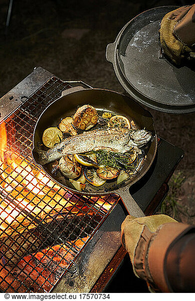 Chef cooking trout in a cast iron over an open fire.