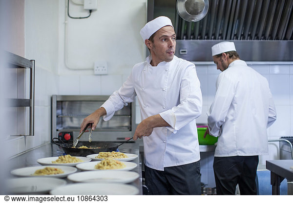 Chef filling plates with pasta in kitchen