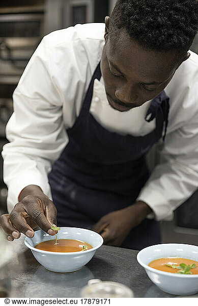 Chef garnishing soup with basil leaves in restaurant kitchen