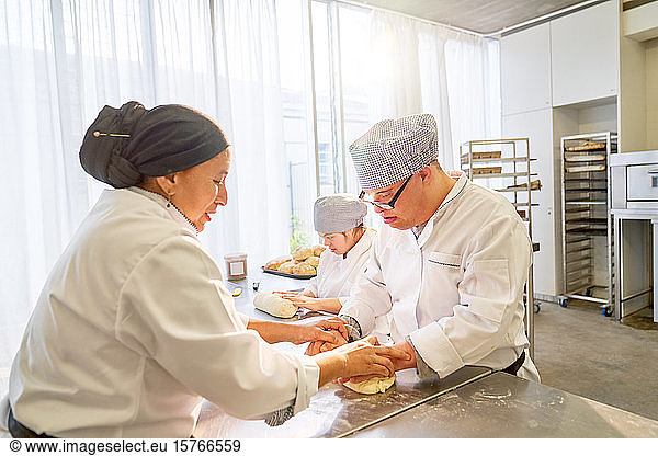 chef-helping-down-syndrome-students-roll-dough-in-kitchen-chef-helping