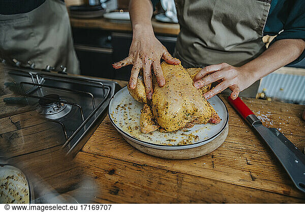 Chef marinating chicken meat while standing by colleague in kitchen