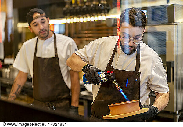 Chef using flaming torch standing with colleague at restaurant