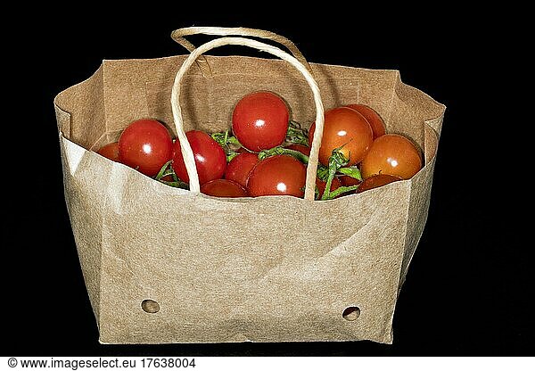 Cherry tomatoes (Solanum lycopersicum var. cerasiforme) on the panicle  lying in a small paper bag  studio photograph with black background