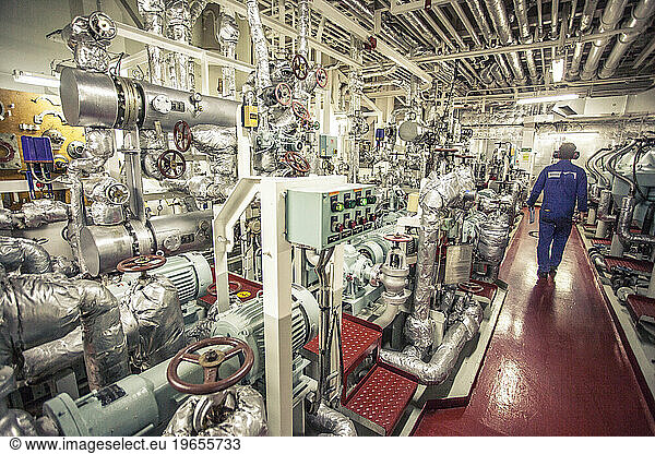 Chief engineer of a container ship walking through a room with generators and life support systems.