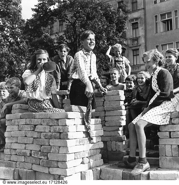 Child / Children’s Life. Children playing amongst piles of bricks and watching bicycles racing on a track they built themselves. Photo  8. August 1953.