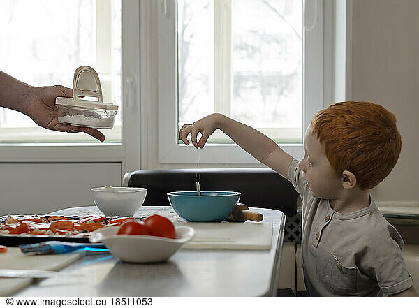 Child cooks with dad. The kid pours salt into a plate.