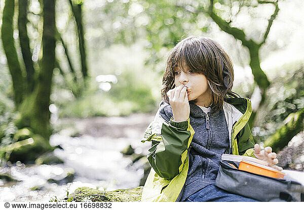 Child eating in the middle of a hiking by forest