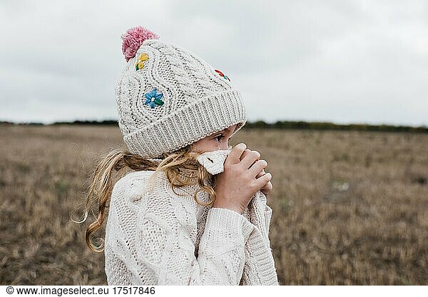 child hiding behind her sweater in a field looking into the distance