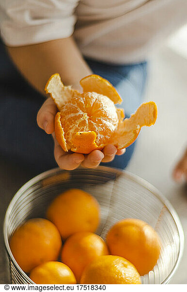 child holds peeled tangerine in hand over basket