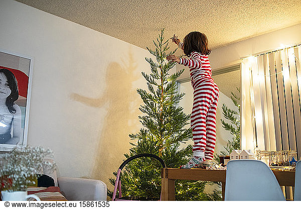 Child in pajamas setting up christmas star on tree at home