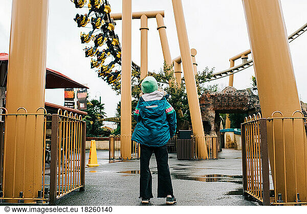 child looking up at a rollercoaster ride in an amusement park