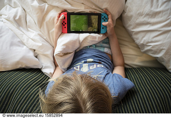 Child Lounging in Bed Playing Hanheld Video Game