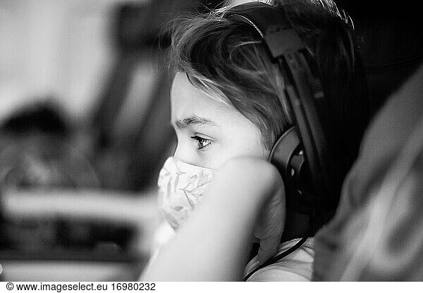 Child on a plane with head phones and wearing a mask.
