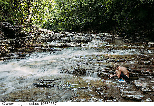 Child playing at base of tiered waterfall in idylllic forest lan