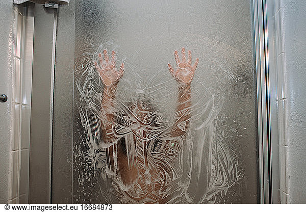 Child playing with soap on shower door with hands