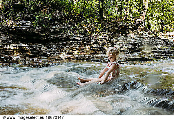 Child sitting in tranquil scenic flowing waterfall in woodland s