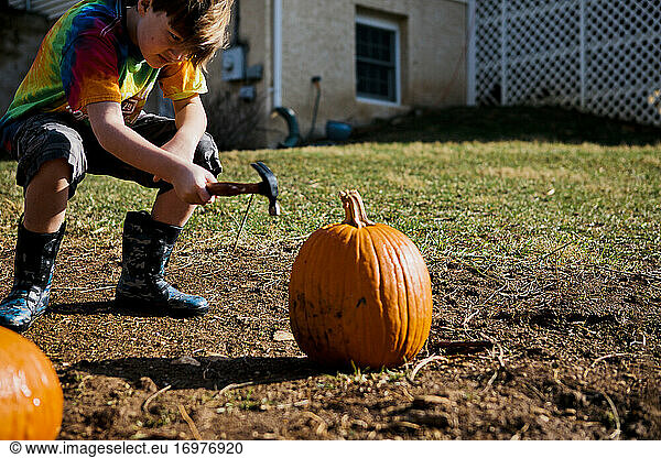 Child swings a hammer at a pumpkin