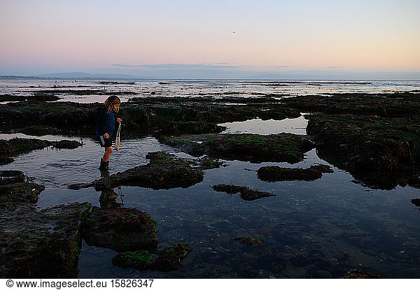Child walking through tide pools at sunset carrying bag