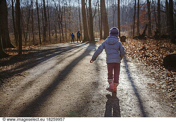 Child walks on sunlit tree-lied path with family in woods