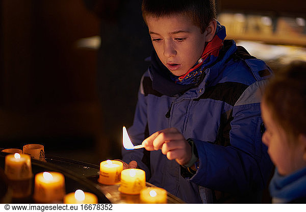 child with a match is going to light a candle inside a church
