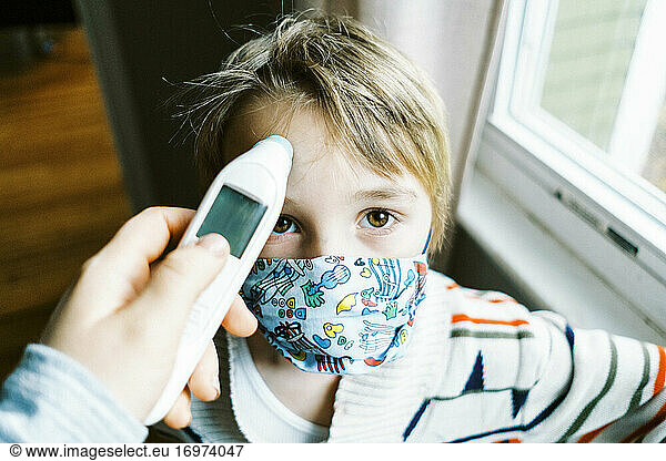 Child with fever wearing mask in home getting temperature taken