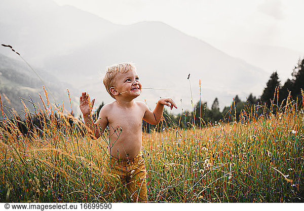 Child with grass in his mouth smiling in the Alps