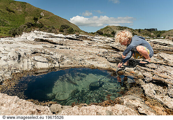 Child with net playing in clear water rock pool