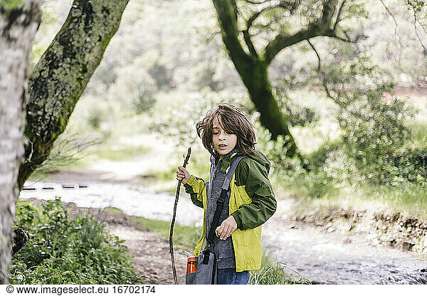 Child with walking stick with apple wearing raining coat by rainforest