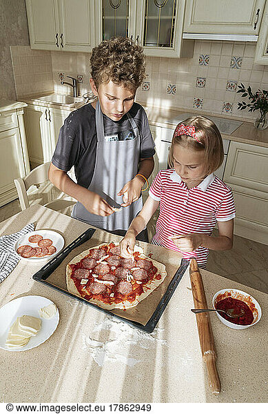 Children cook pizza together at home in the kitchen.