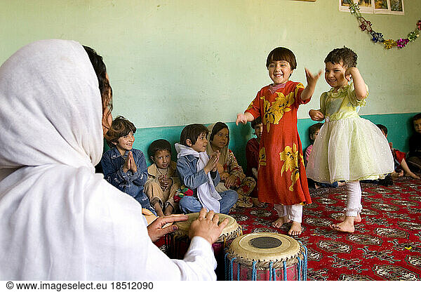 Children dance at a Kabul preschool while their teacher drums a rhythm.