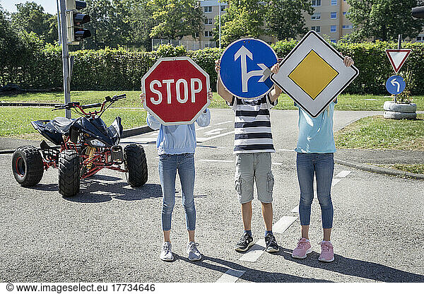 Children holing road signs in front of face standing on road