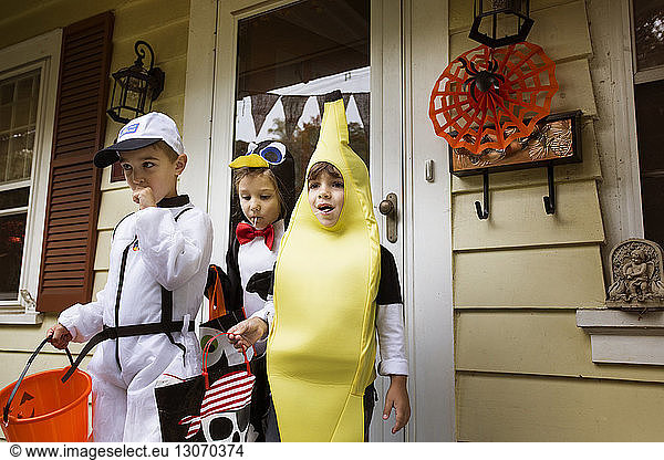 Children in Halloween costumes standing against house during trick or treating