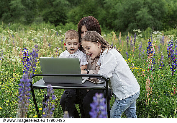 Children looking at mother working on laptop in meadow
