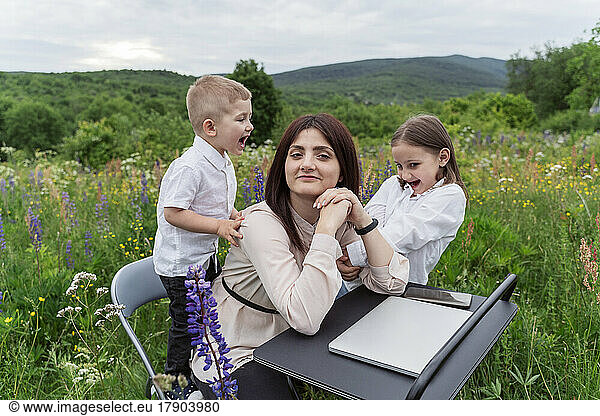 Children playing with mother at desk in field