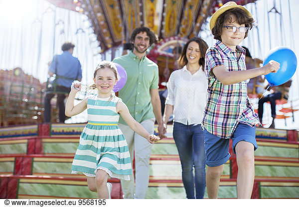 Children running in front of carousel  parents following them
