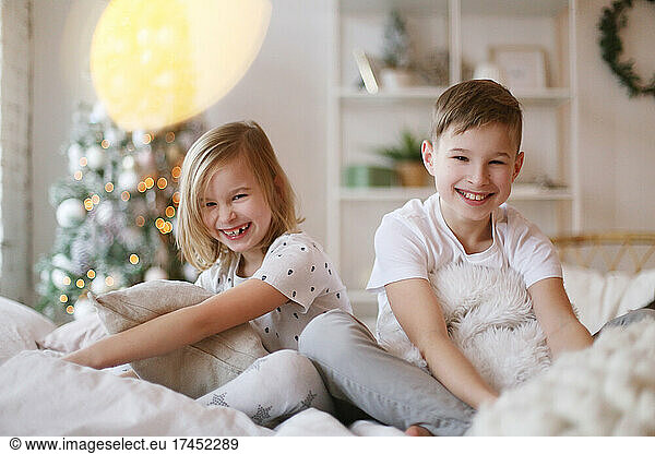 Children sit on the bed and look at the camera smiling.