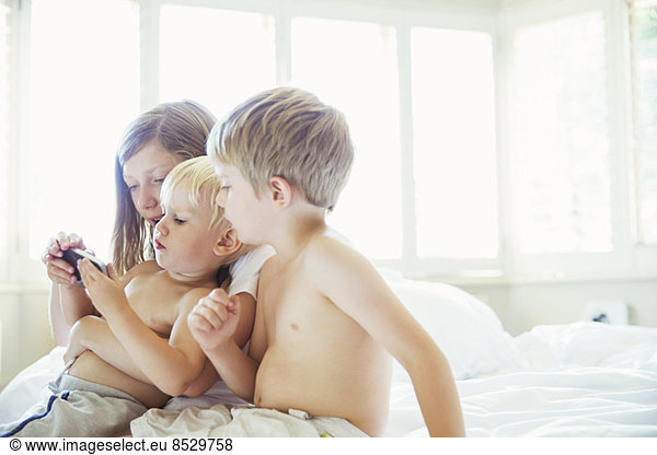 Children using cell phone on bed