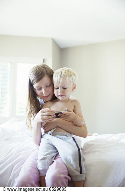 Children using cell phone together on bed