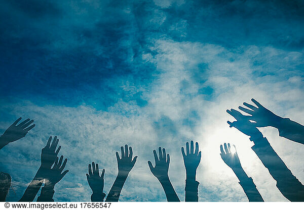 Childrens hands reaching into the blue and clouds sky
