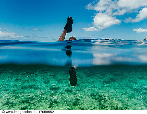 Childs feet snorkeling in clear ocean water with blue sky