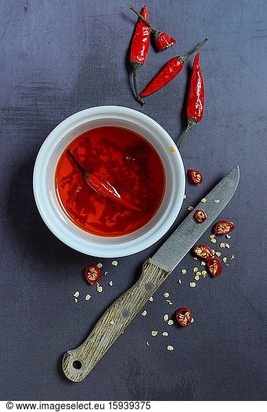 Chili oil in bowl with knife and chili peppers  food photography  studio shot  Germany  Europe