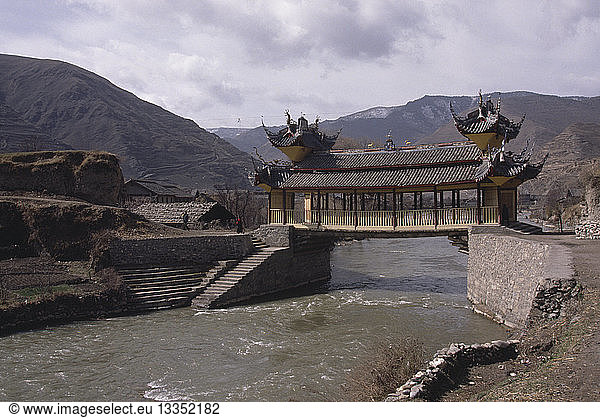 CHINA Sichuan Province Songpan Chinese bridge with pagoda style roof over river in mountain landscape