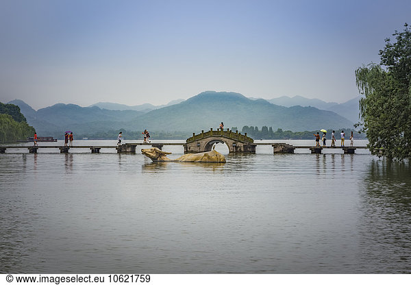 China  Zhejiang  Hangzhou  Riesige goldene Wasserbüffel und Fußgänger auf einer Brücke am Westsee