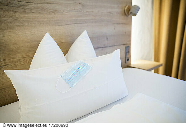 Chirurgische Maske auf weißem Kopfkissen über dem Bett