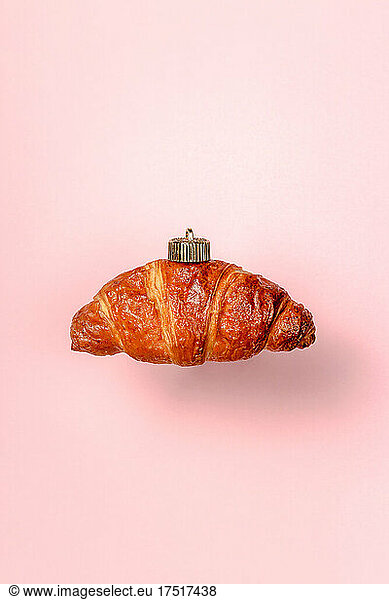 Christmas bauble decoration of croissant on pink. New year concept.