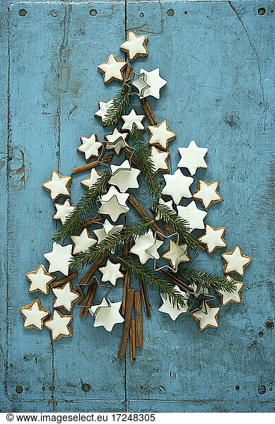 Christmas cinnamon star shaped cookies together with cinnamon and needle branches arranged in Christmas Tree on blue rustic wooden background